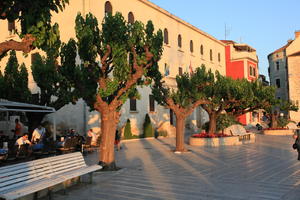 bench, building, Croatia, dusk, evening, eye level view, group, Makarska, object, people, plaza, sitting, Splitsko-Dalmatinska, tree, vegetation